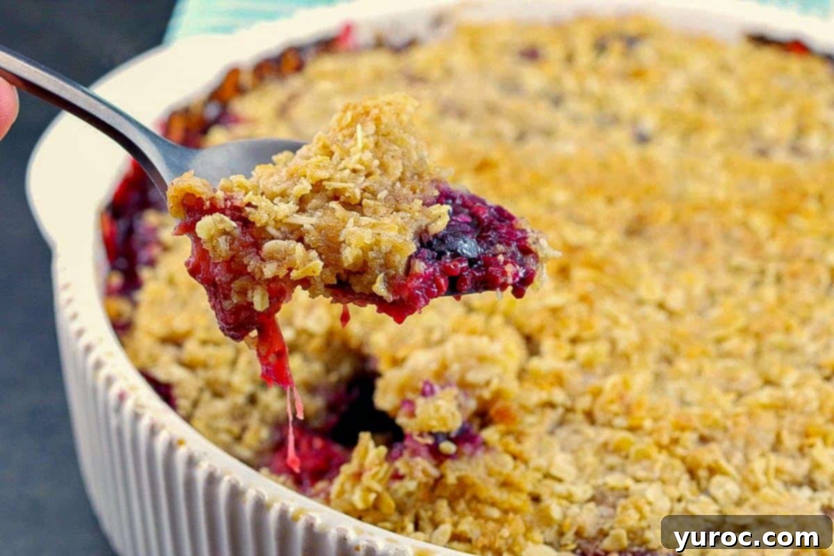 Zesty Triple Berry Crisp in a white baking dish being spooned out.