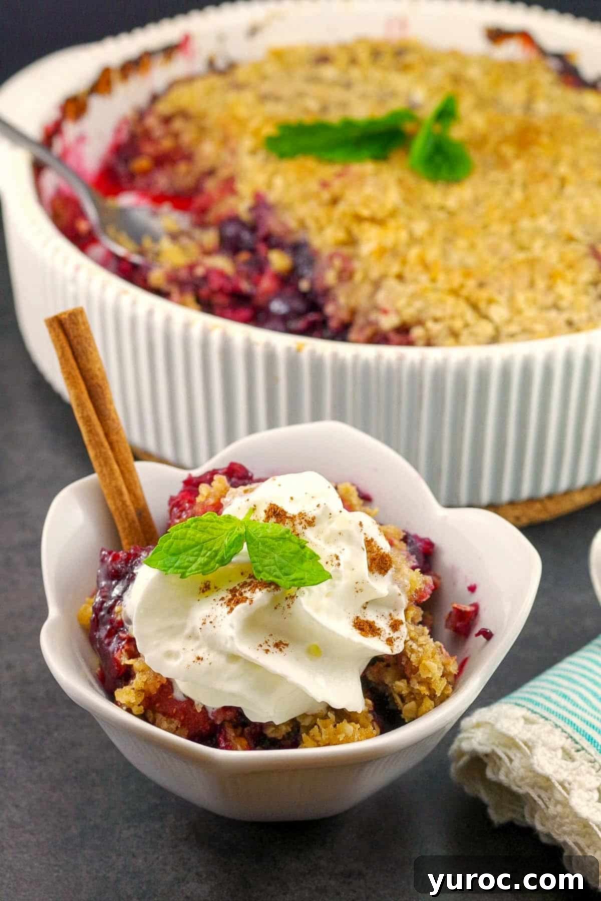 Triple Berry Crisp in a white bowl with a baking dish full of Triple berry crisp in the background.