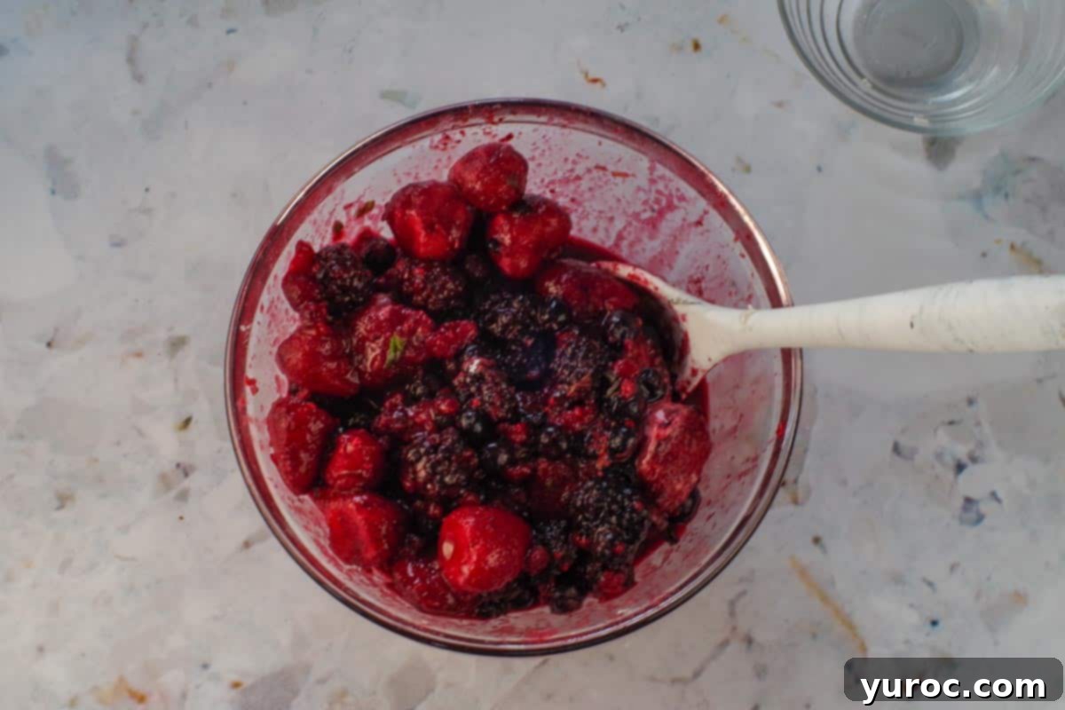 Berries mixed and coated with other ingredients in glass bowl with spoon.