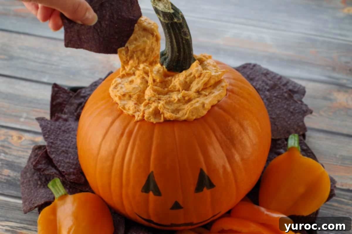 black nacho chip being dipped into Halloween Buffalo Chicken Dip on a black platter with black nacho chips and orange peppers