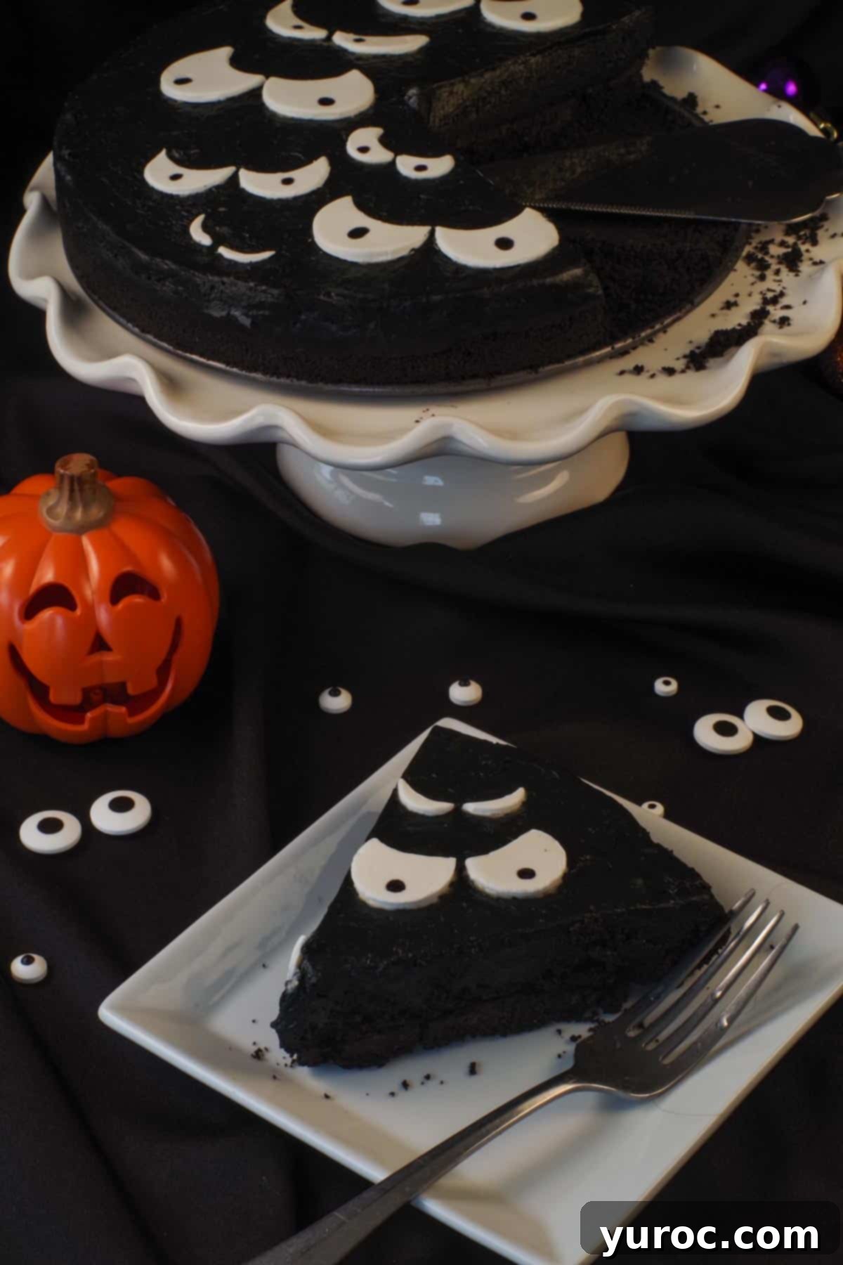A slice of Halloween Party Cheesecake in front of a jack-o-lantern and a white cake stand with remaining cake in the background