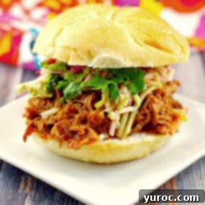 slow cooker pulled pork sandwich on a white plate with a colorful tea towel in the background