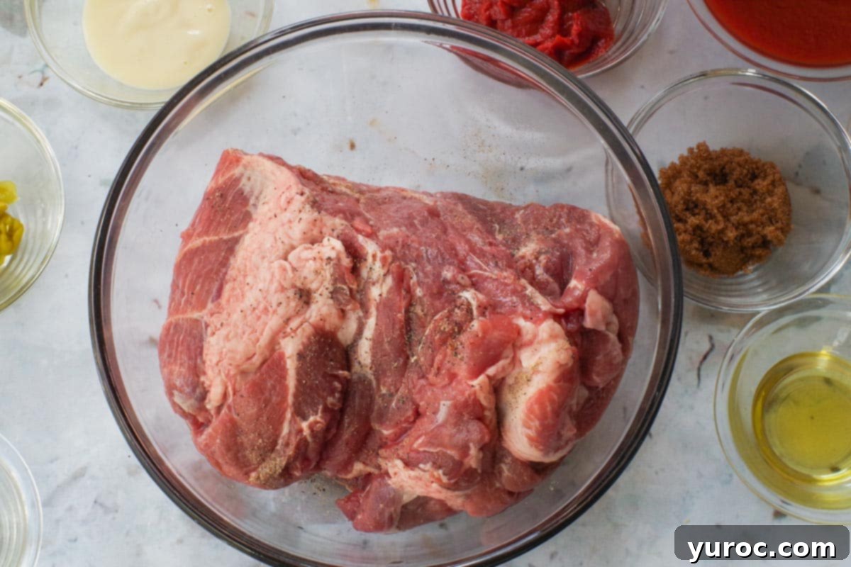 Pork shoulder in a glass bowl, sprinkled with salt and pepper.