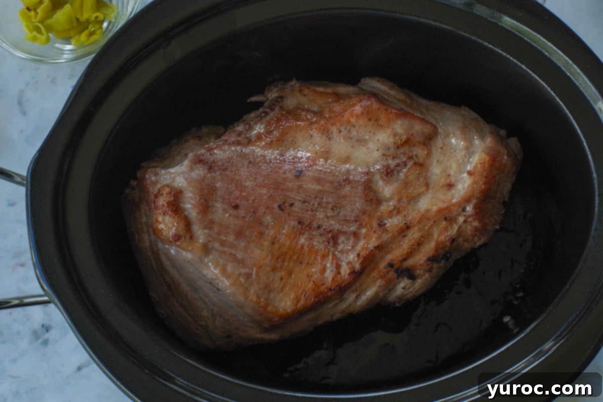 Browned Pork Shoulder transferred to a slow cooker.