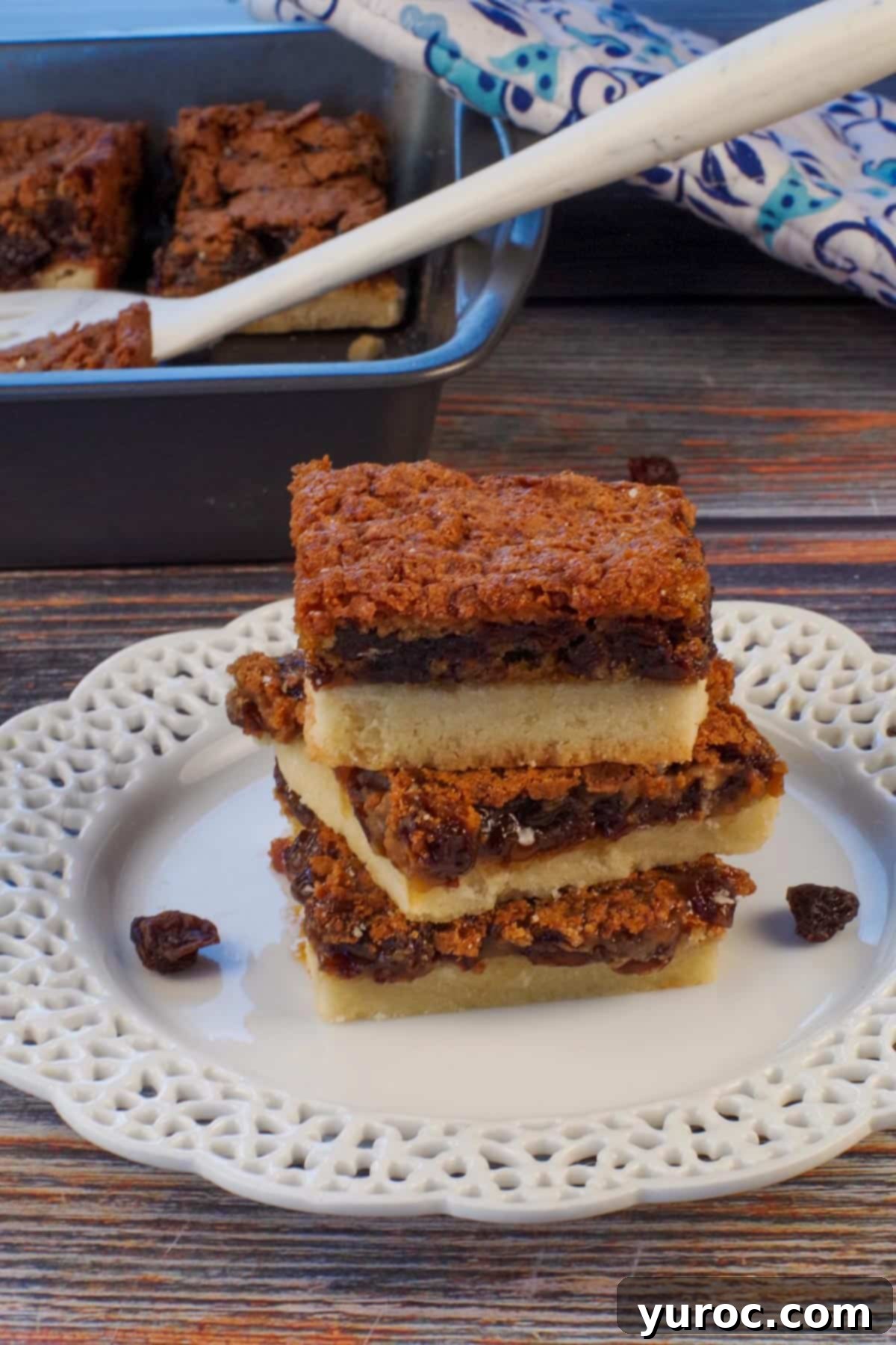 Three golden butter tart slices artfully arranged on a white plate, with a pan of more squares visible in the softened background.
