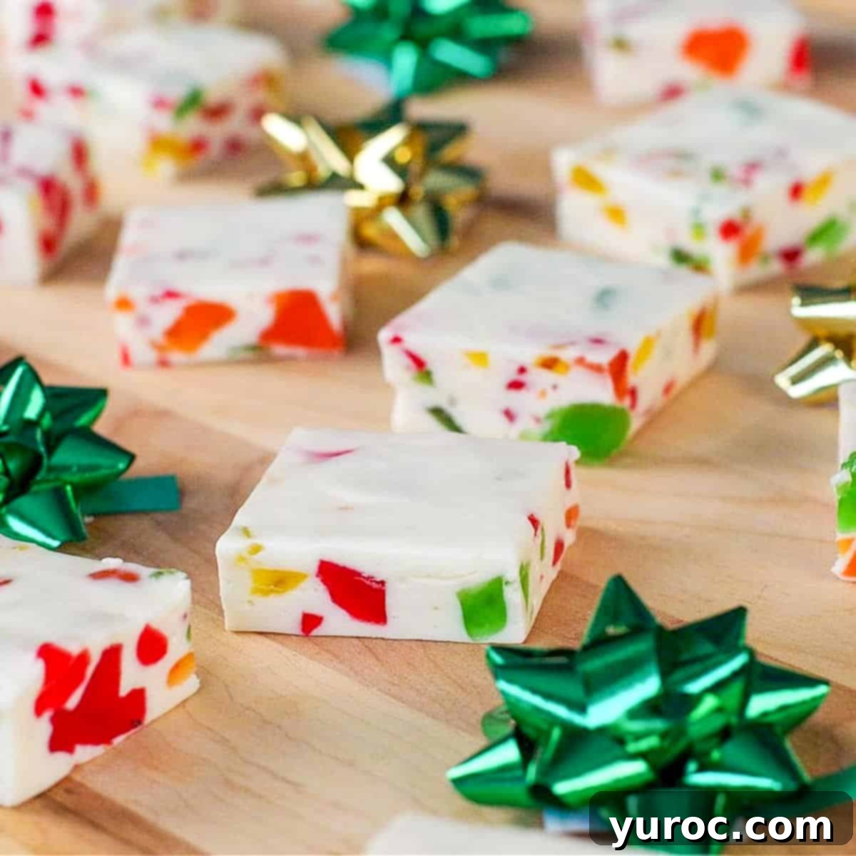 Assortment of Christmas nougat candy, cut into neat squares, arranged on a rustic wooden cutting board with charming green and gold mini bows for decoration.