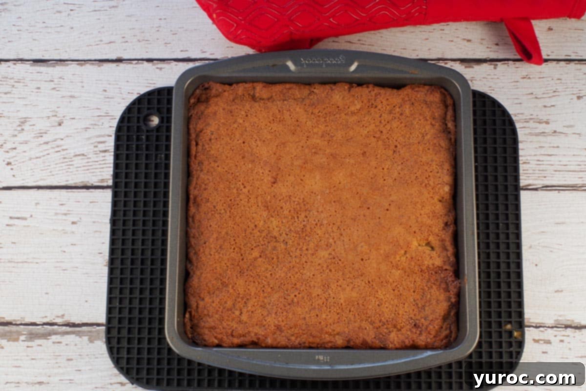 The finished baked butter tart slice in the pan, on a black trivet, with a golden brown top.
