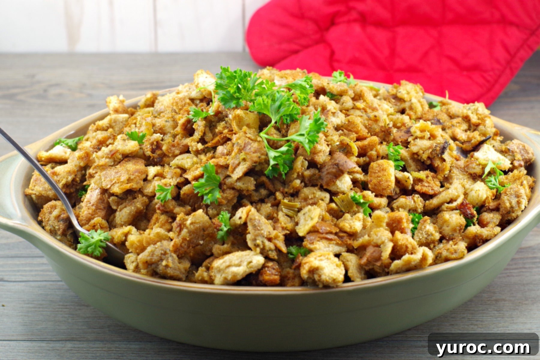 Old fashioned bread stuffing displayed in a rustic green dish, with a serving spoon.