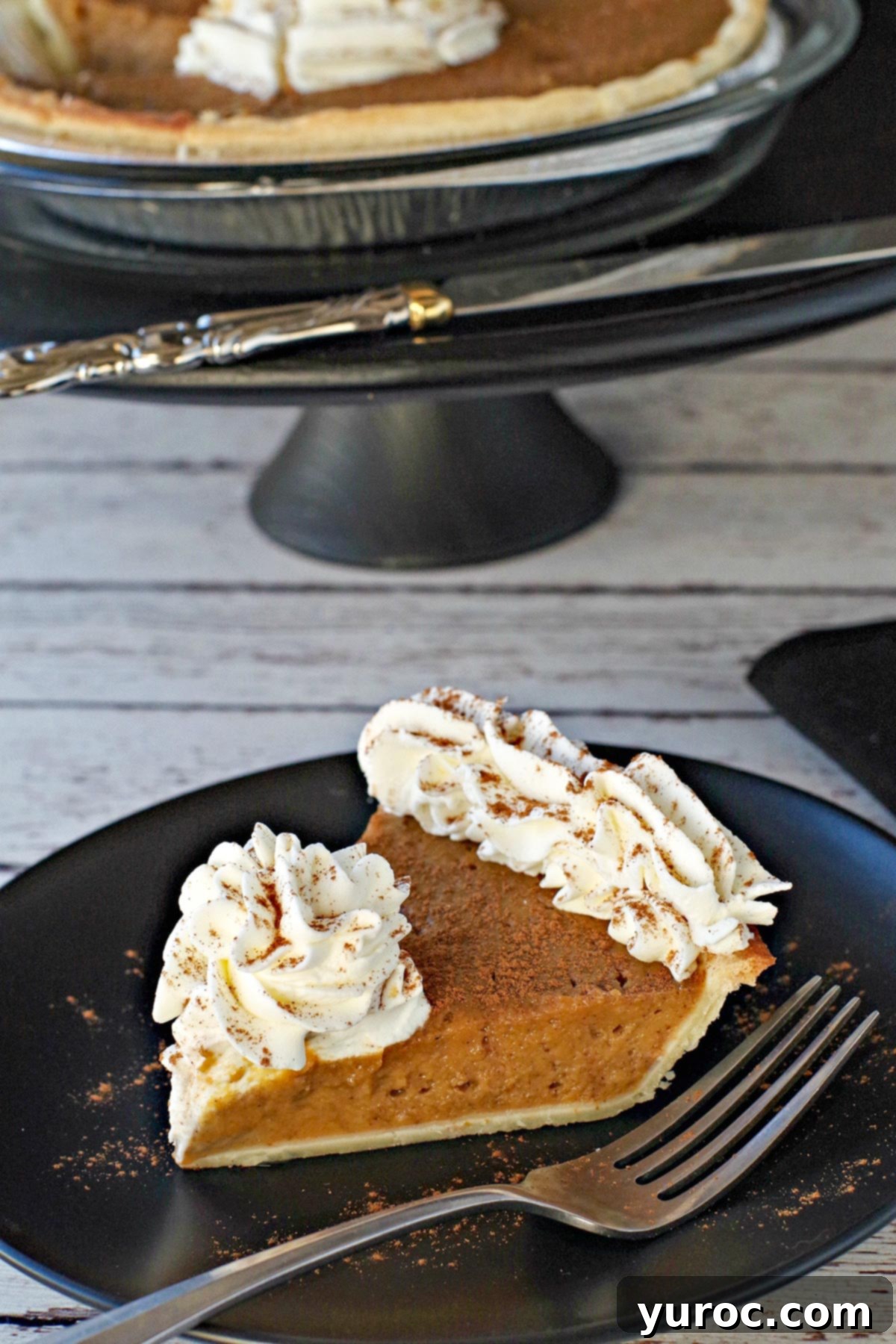 Prize-Winning Canned Pumpkin Pie 3 Another enticing view of a slice of pumpkin pie, crowned with whipped cream, on a black plate. The background features a larger pie on a black platter, highlighting its festive presentation.