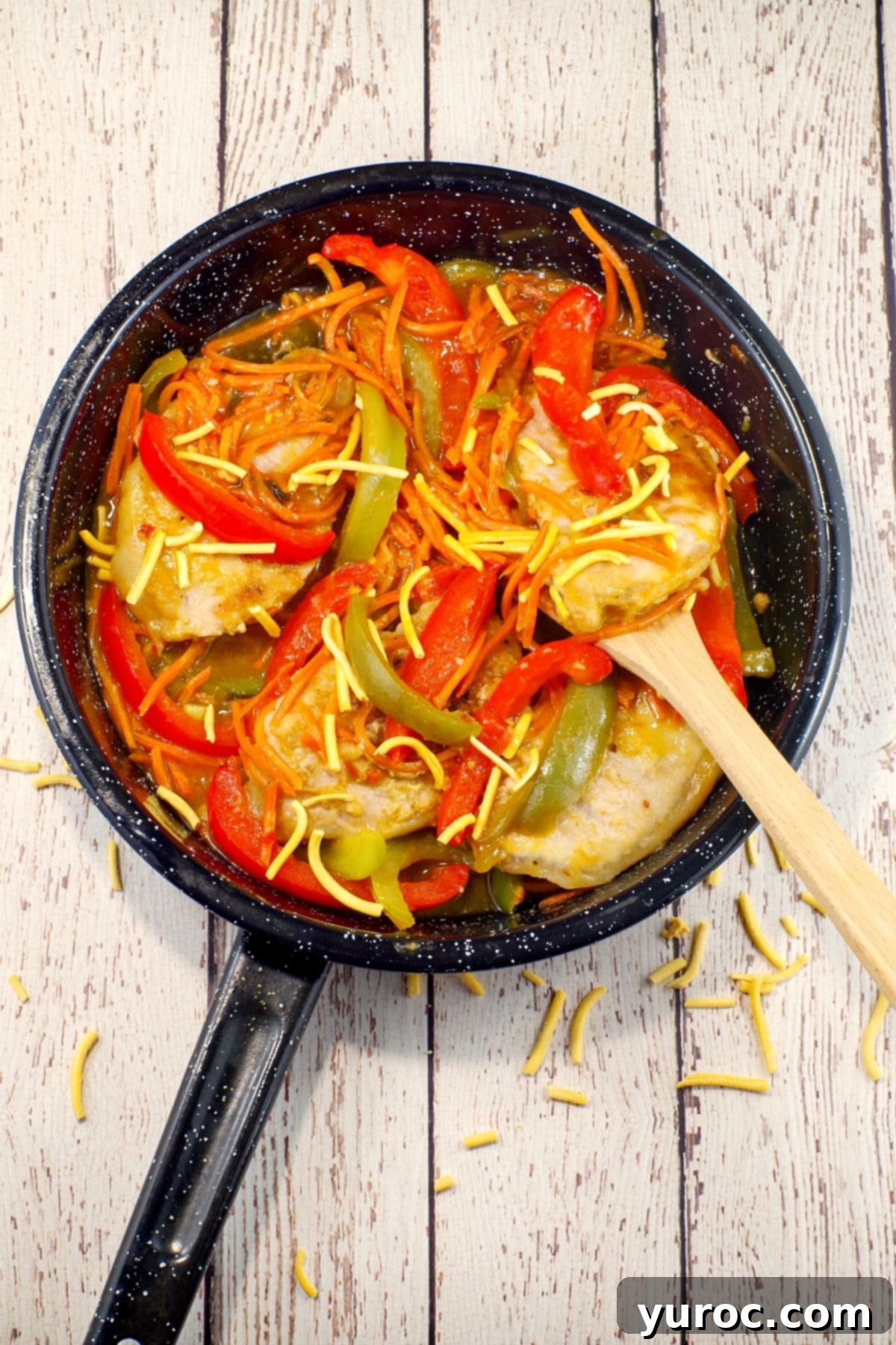 Plum pork chops in a speckled black frying pan on a white surface with scattered chow mein noodles, highlighting the one-pan convenience.