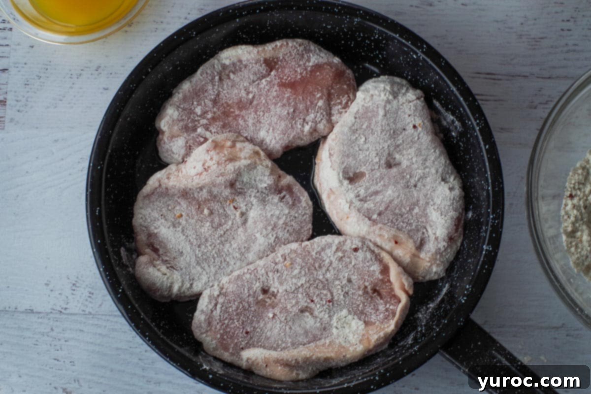 Four pieces of flour-coated pork loin chops placed in the hot skillet.