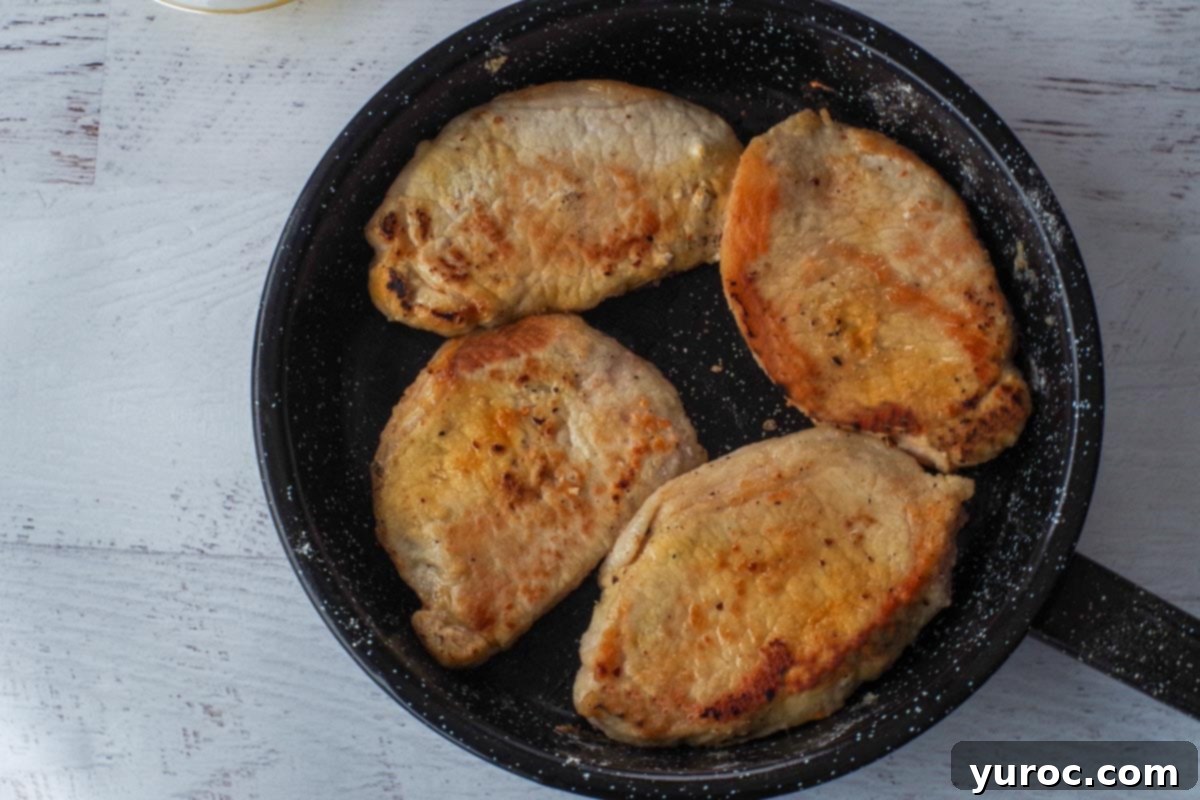 Four browned pork chops cooking in the frying pan.
