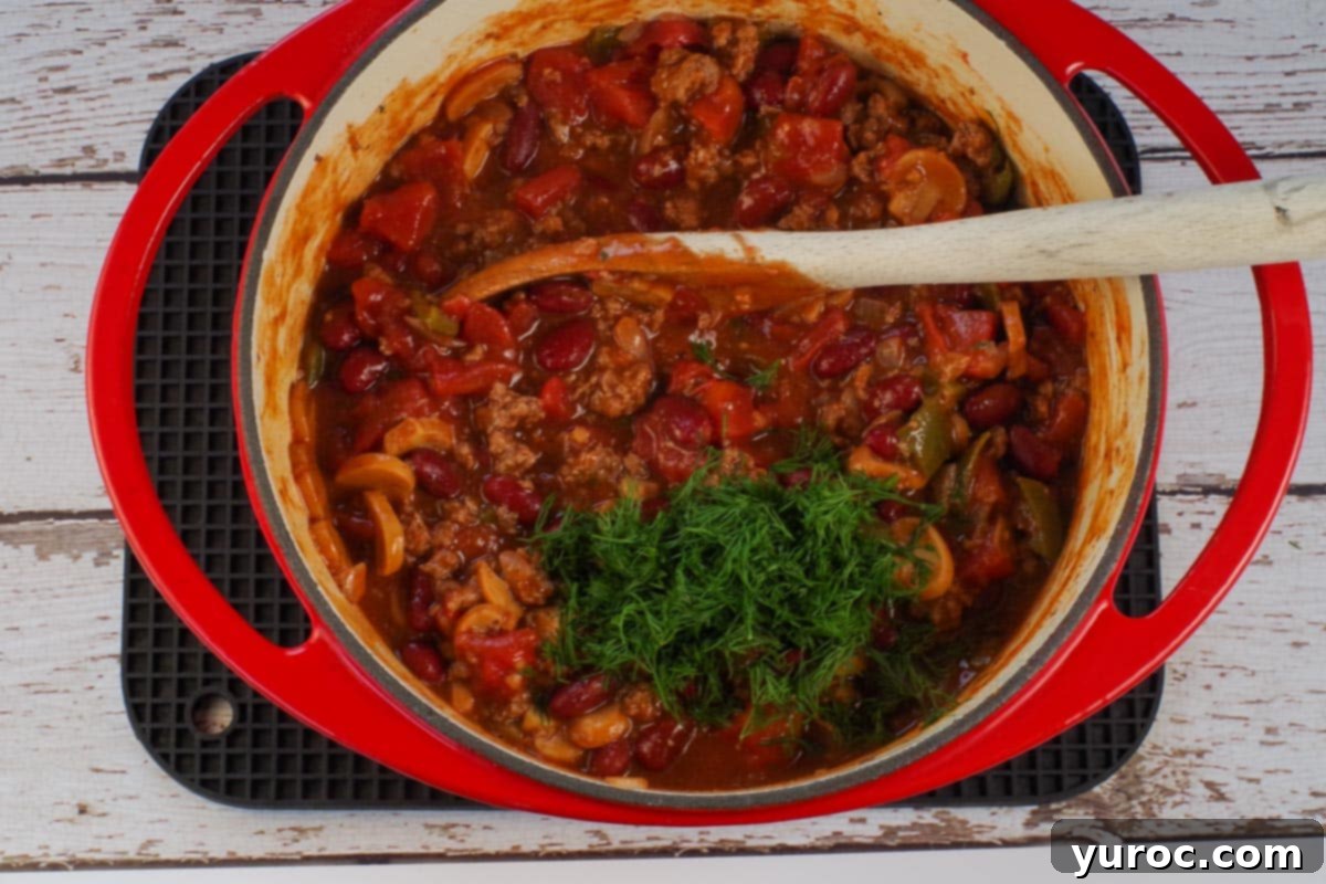 fresh dill added to beef and pork chili in orange dutch oven