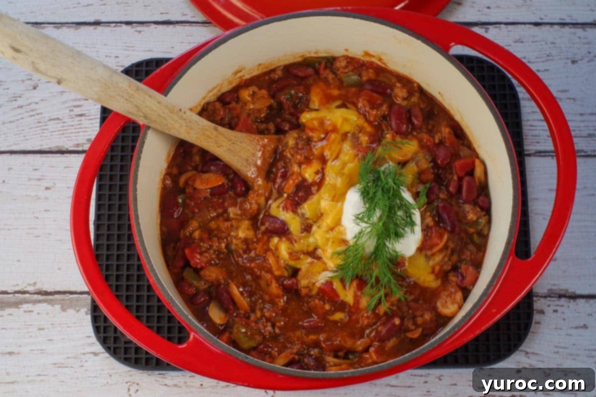 chili in orange dutch oven, garnished with cheese, dill and sour cream.