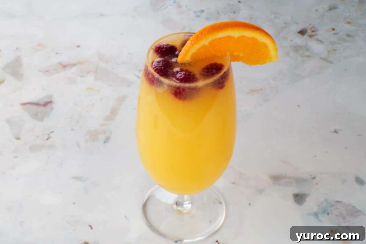 Frozen raspberries and orange juice added to glass as garnishes.