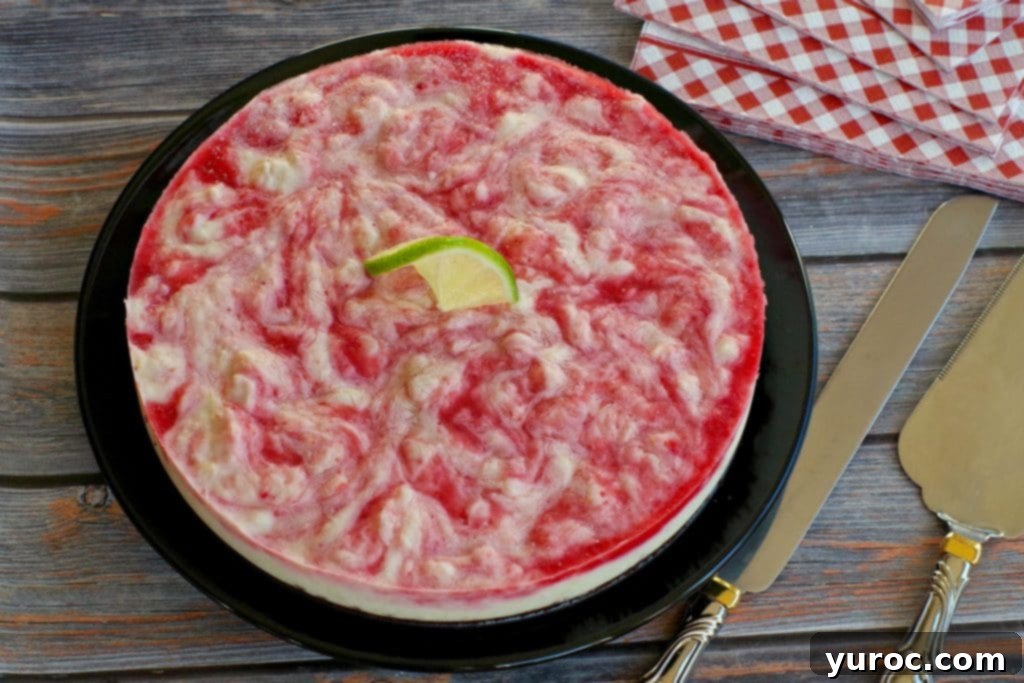 A slice of frozen cheesecake resting on a faux wooden surface, with red and white checkered napkins in the blurred background.