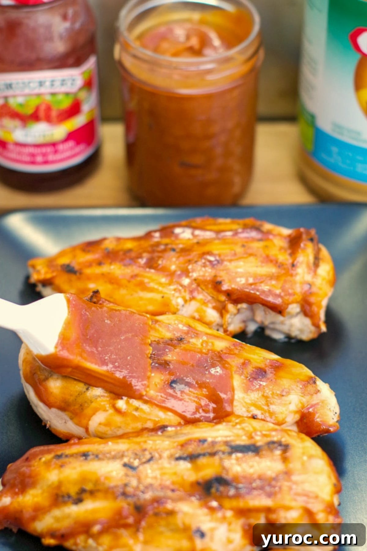 peanut butter BBQ sauce being spread on chicken on a black serving tray with jar of BBQ sauce in background