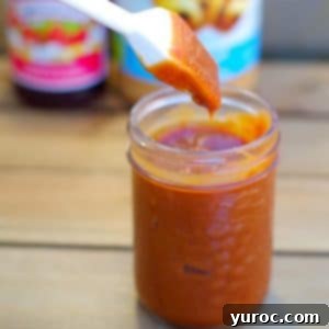 BBQ sauce in a clear jar with brush being dipped in and peanut butter and jam in background