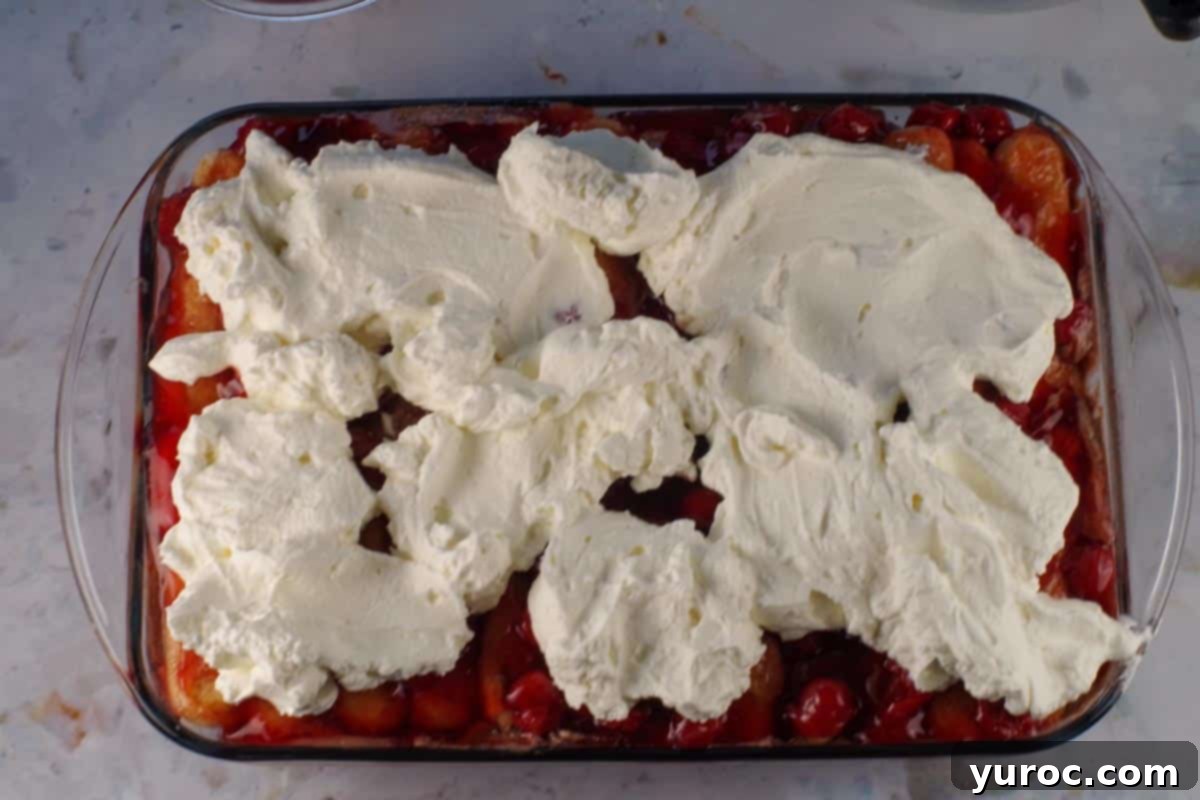Large dollops of whipped cream placed on cherry pie filling layer.