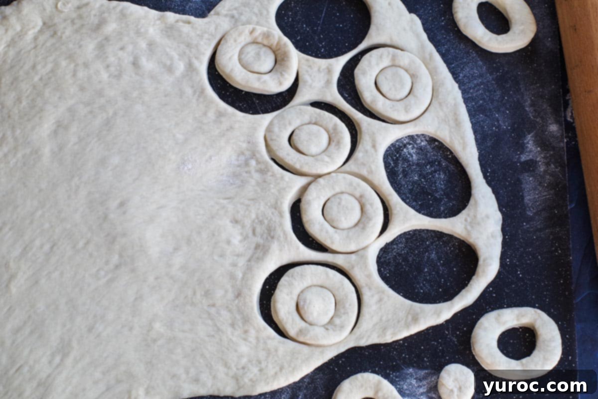 Dough being cut into mini doughnuts with a small cutter on a black cutting board.