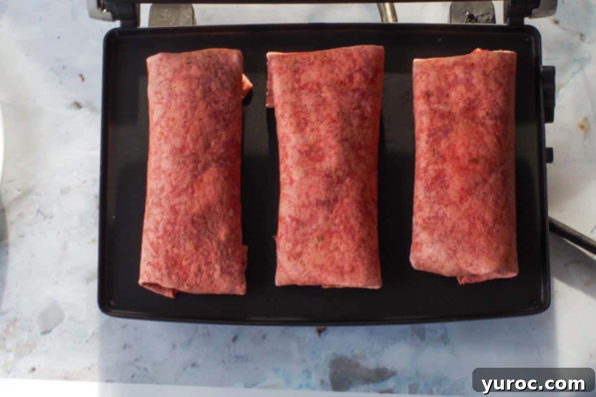 3 breakfast burritos on a panini press ready for grilling
