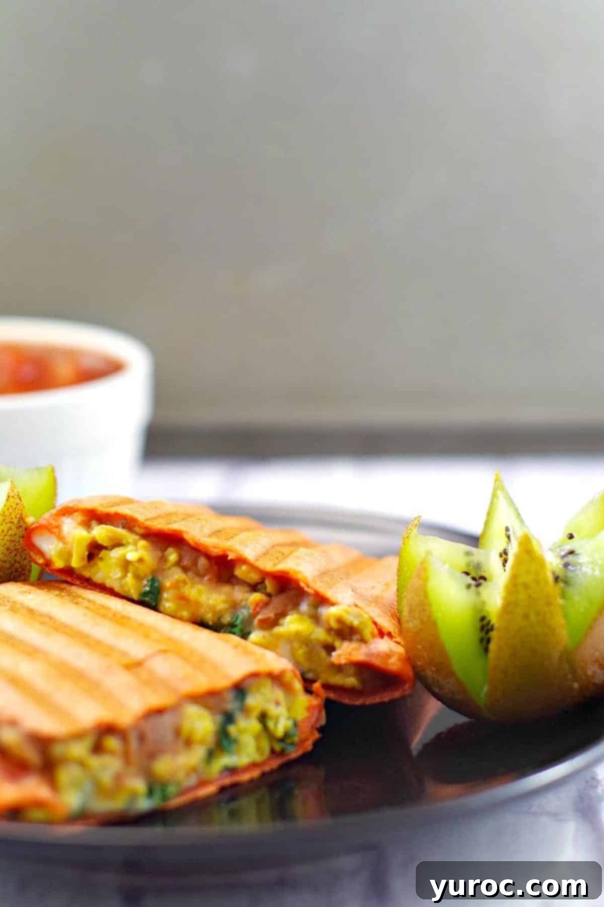 Mediterranean breakfast burrito, cut in half on a black plate with a kiwi flowere and salsa in a white dish.