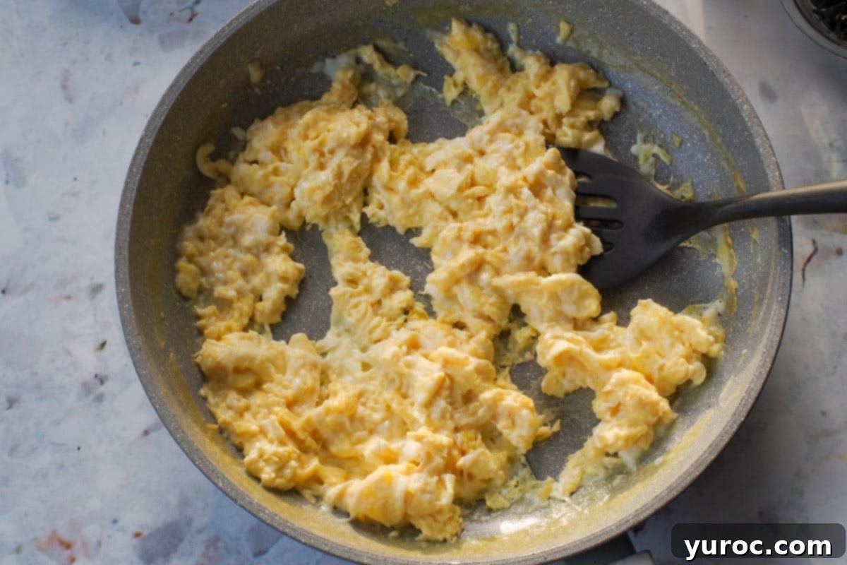 Scrambled eggs in a fryng pan with a black spatula flipper.