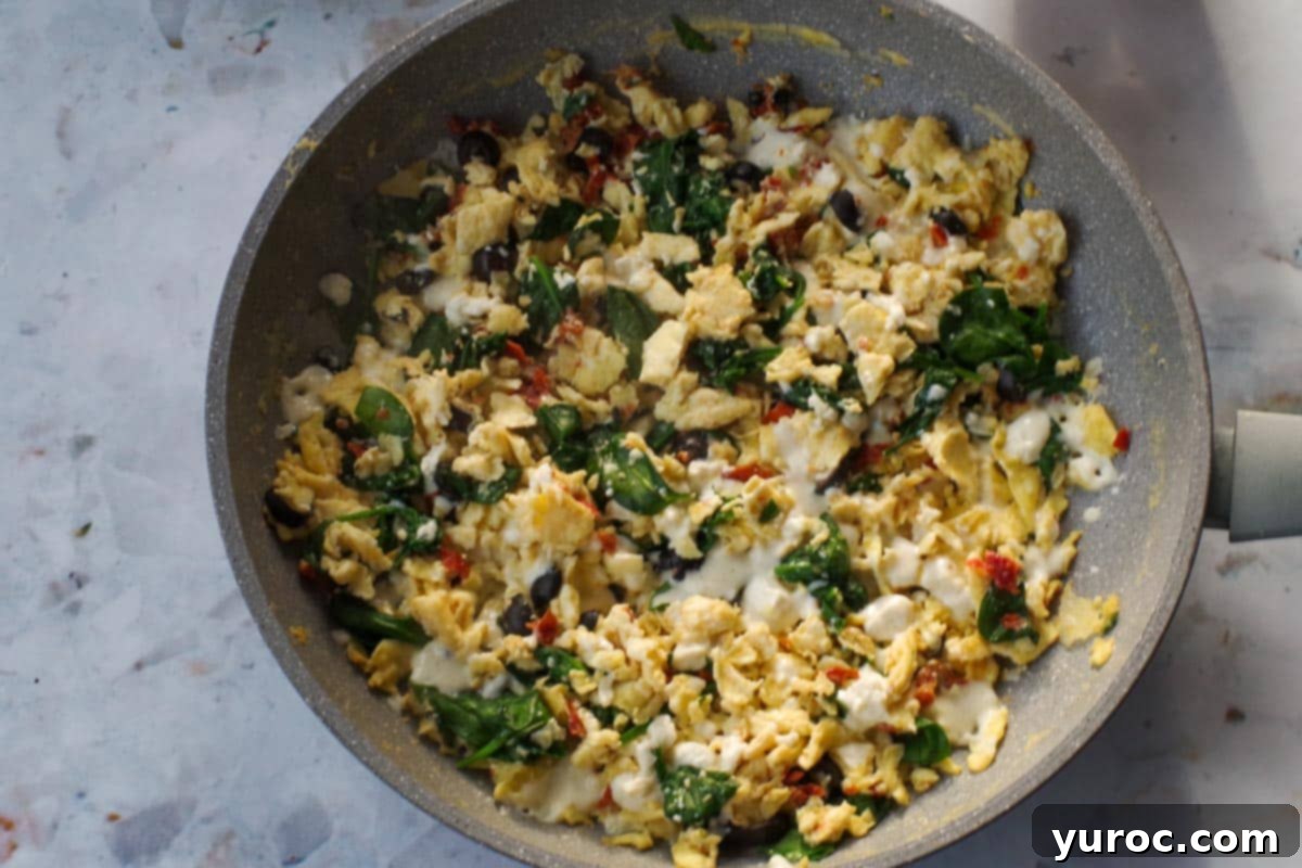 Egg mixture with melted feta cheese in a frying pan.