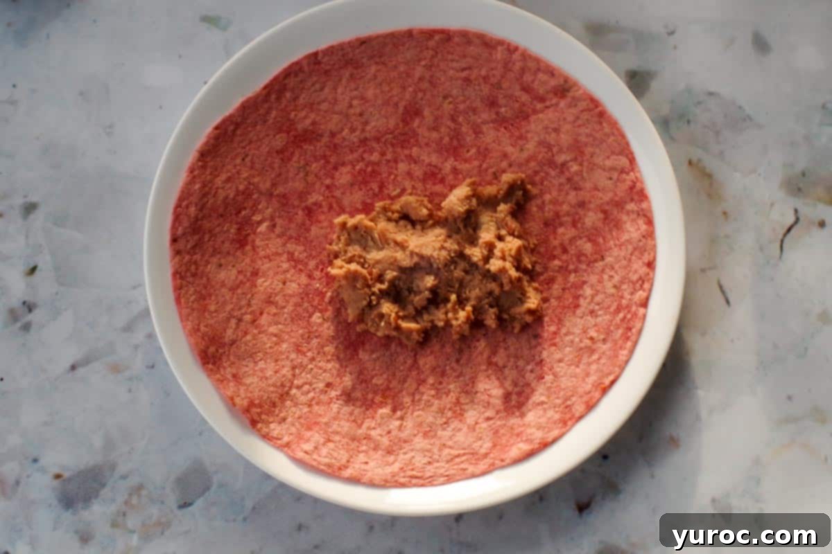 Refried beans added to middle of sun-dried tomato tortilla