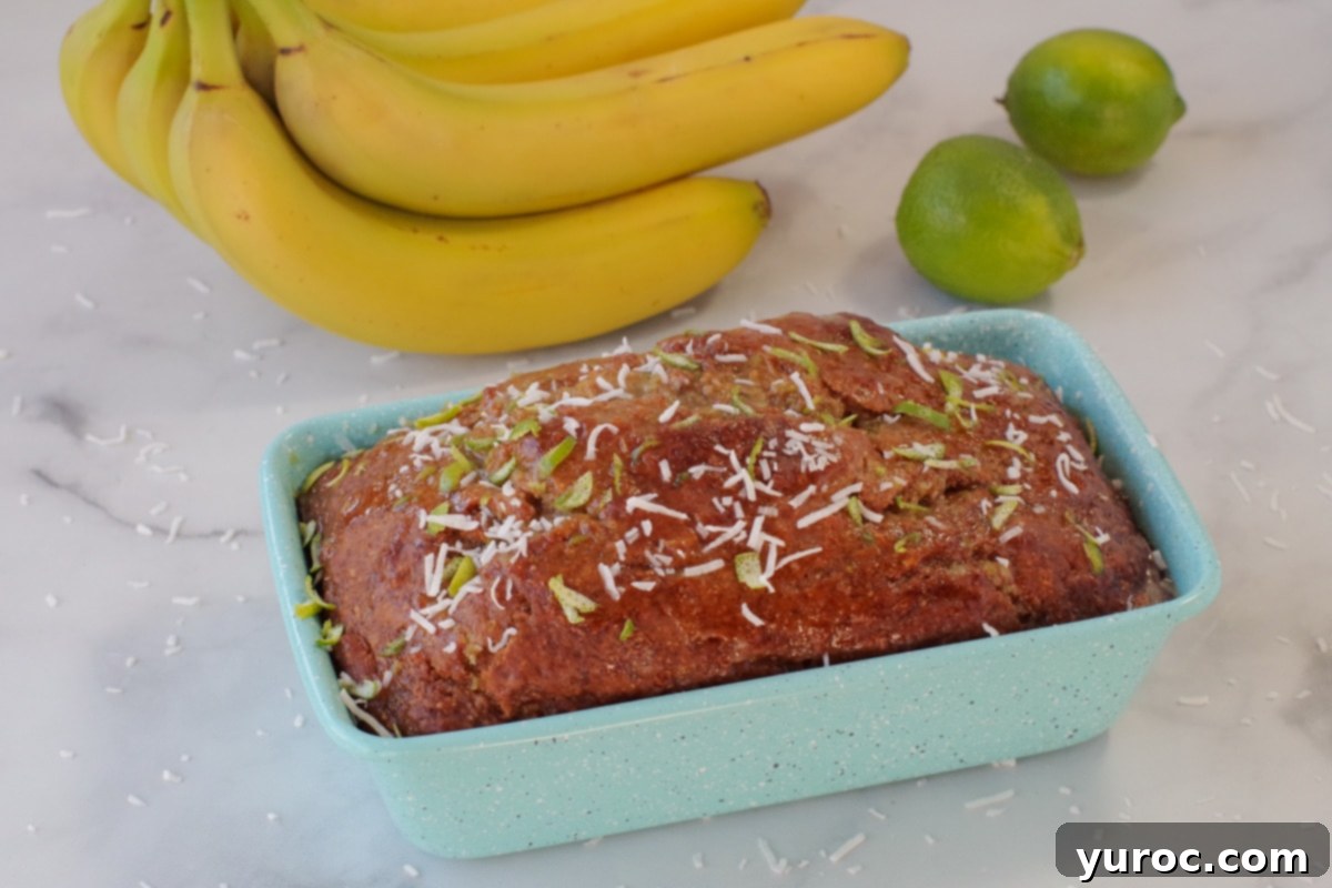 Tropical banana bread in blue loaf pan with fresh bananas and limes in the background