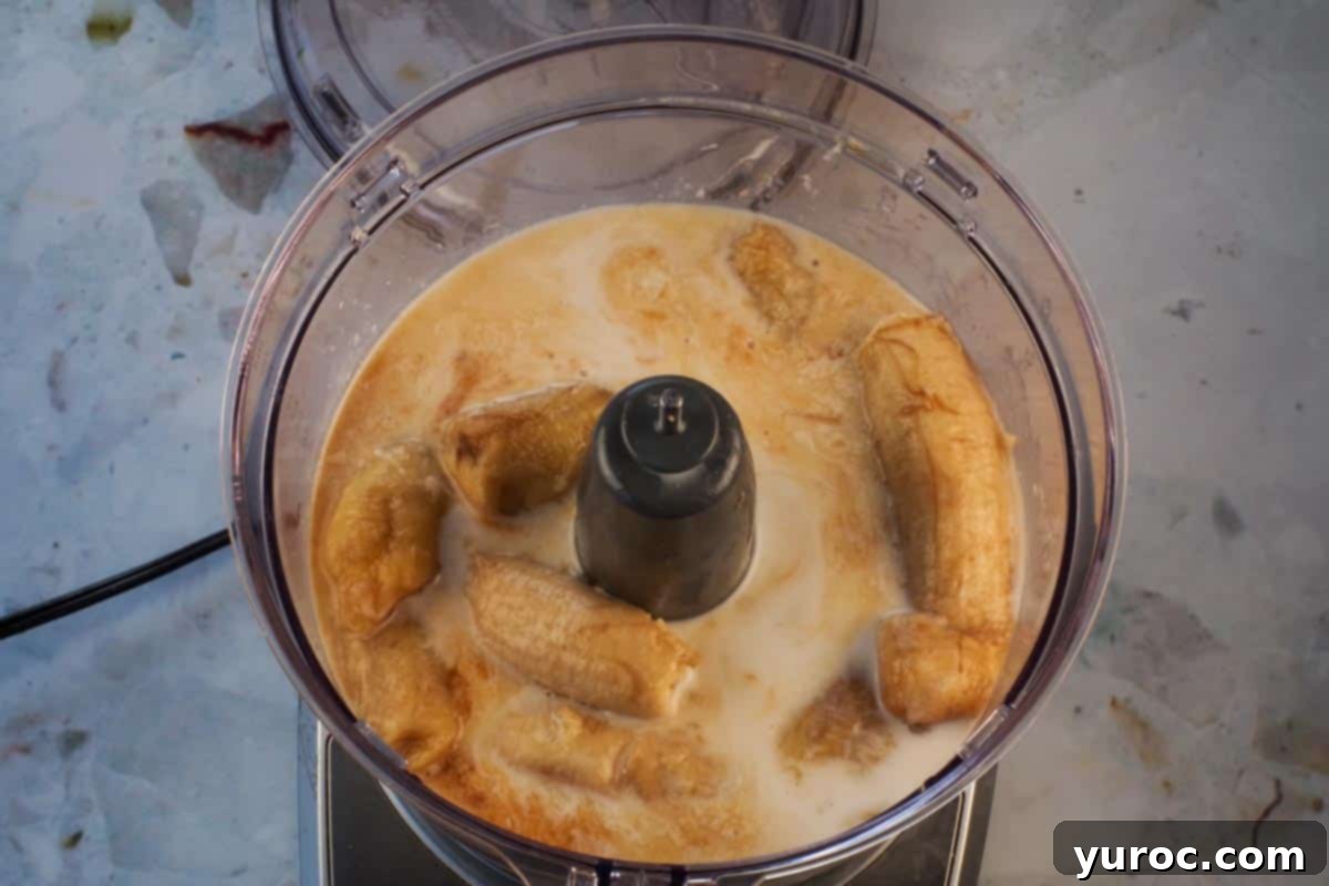 Coconut milk, sliced bananas, vanilla, and amber rum added to a food processor for blending.