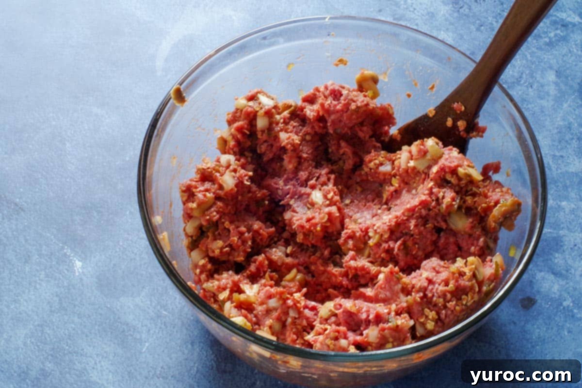 meatloaf ingredients in a large glass mixing bowl with a wooden spoon in bowl