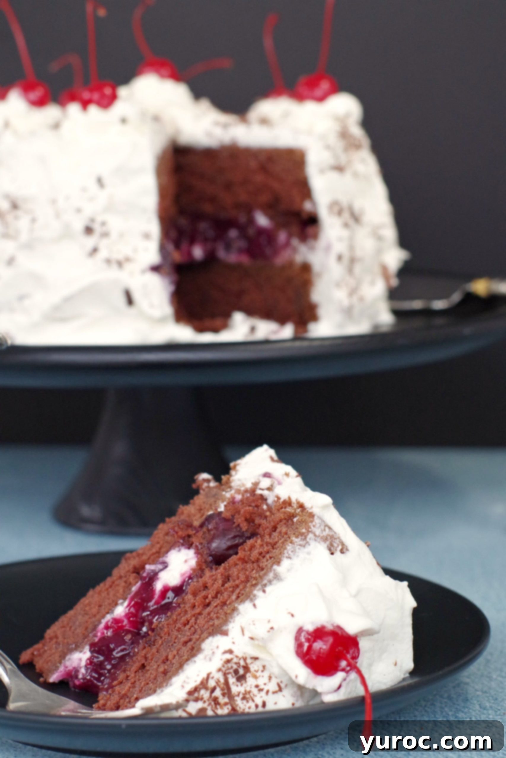 Quick and Easy Black Forest Cake 3 A slice of elegant Black Forest cake on a black plate, with the whole cake visible in the background.