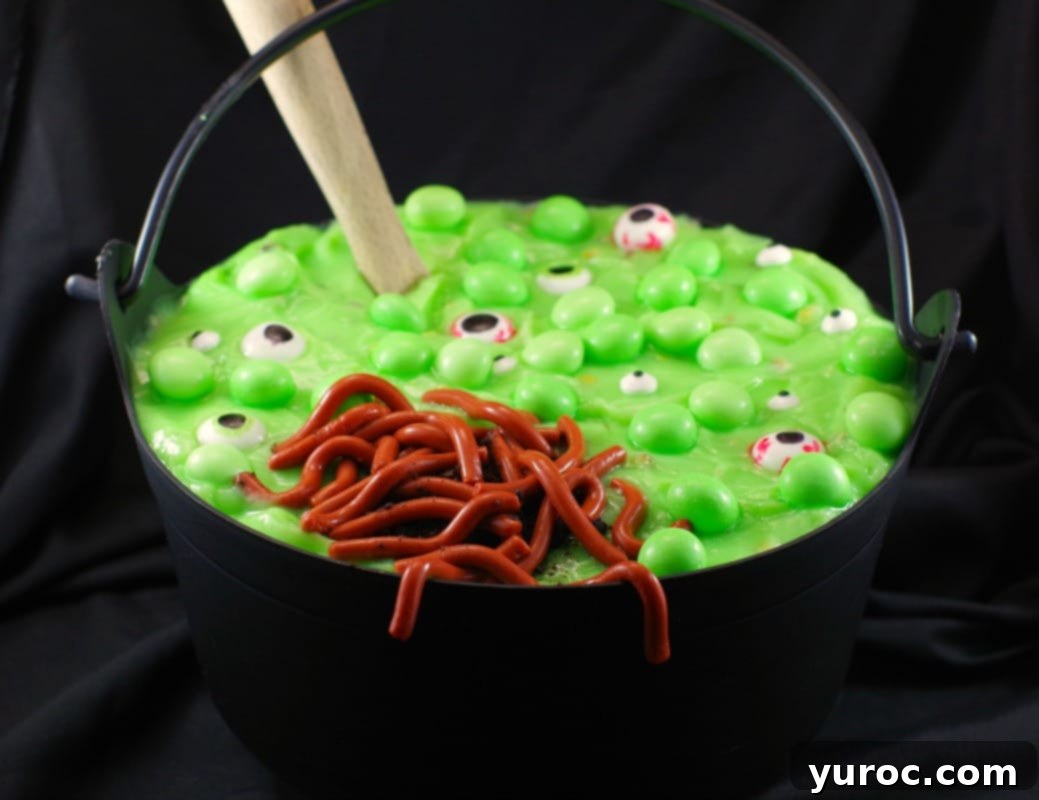 Spooky Swamp Trifle with Wriggling Worms 2 A black plastic cauldron filled with Witches Brew Spumoni Trifle, featuring layers of cake, green pudding, whipped cream, and jello worms, ready for a Halloween party.