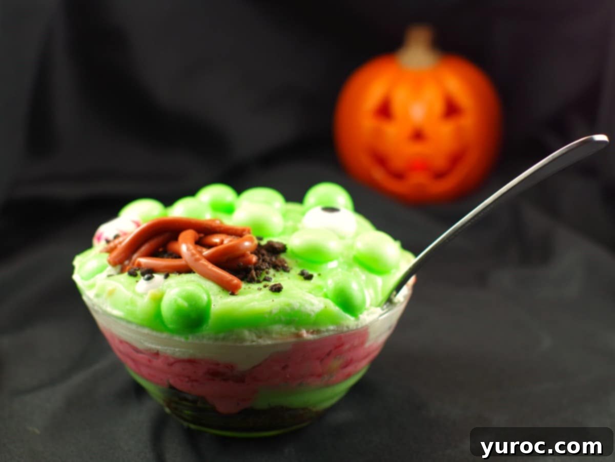 Spooky Swamp Trifle with Wriggling Worms 3 A vibrant Witches Brew Halloween Trifle with layered ingredients, green bubbles, and candy eyes, presented in a clear bowl.