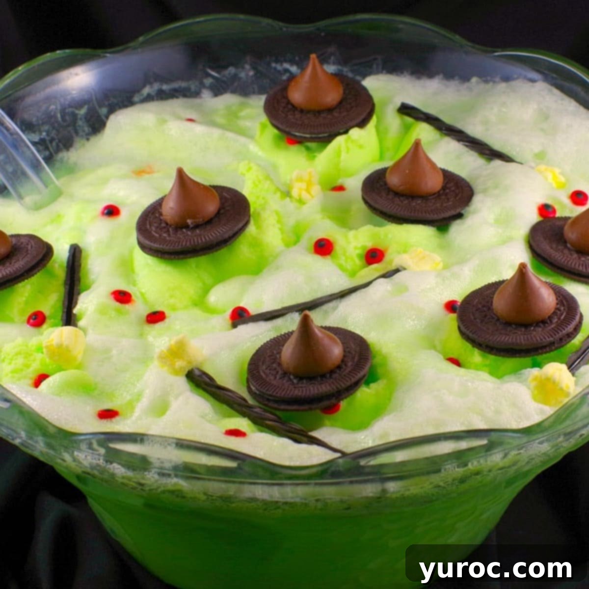Spooky Swamp Trifle with Wriggling Worms 7 A large punch bowl filled with vibrant green Melting Witch Halloween Punch, with black decorative material in the background creating a spooky atmosphere.