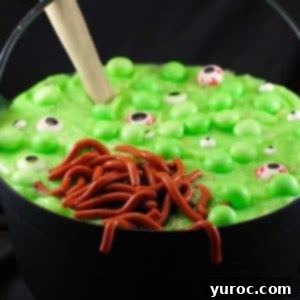 Spooky Swamp Trifle with Wriggling Worms 10 A black cauldron filled with Witches Brew Halloween Trifle, featuring jello worms, mint eyeballs, and a wooden spoon, creating a spooky and delicious dessert.