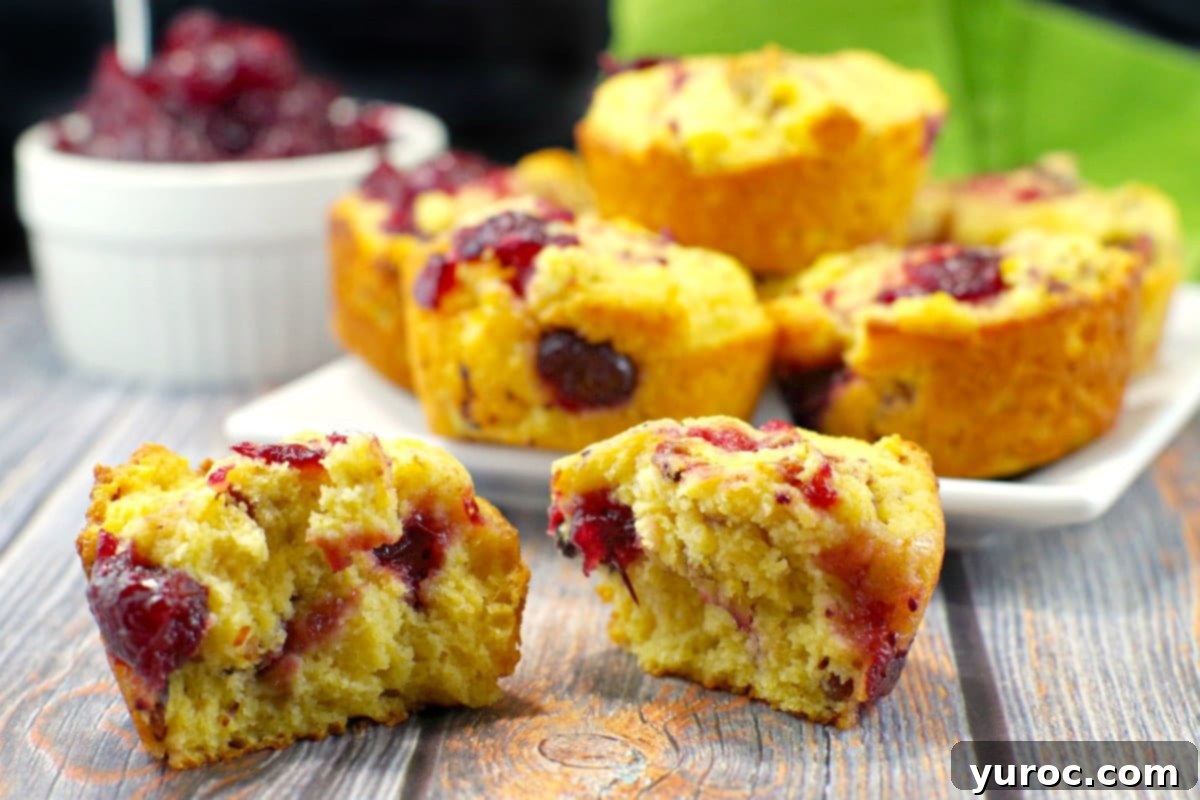 cranberry cornbread muffin spilt in half with a plate of muffins in background