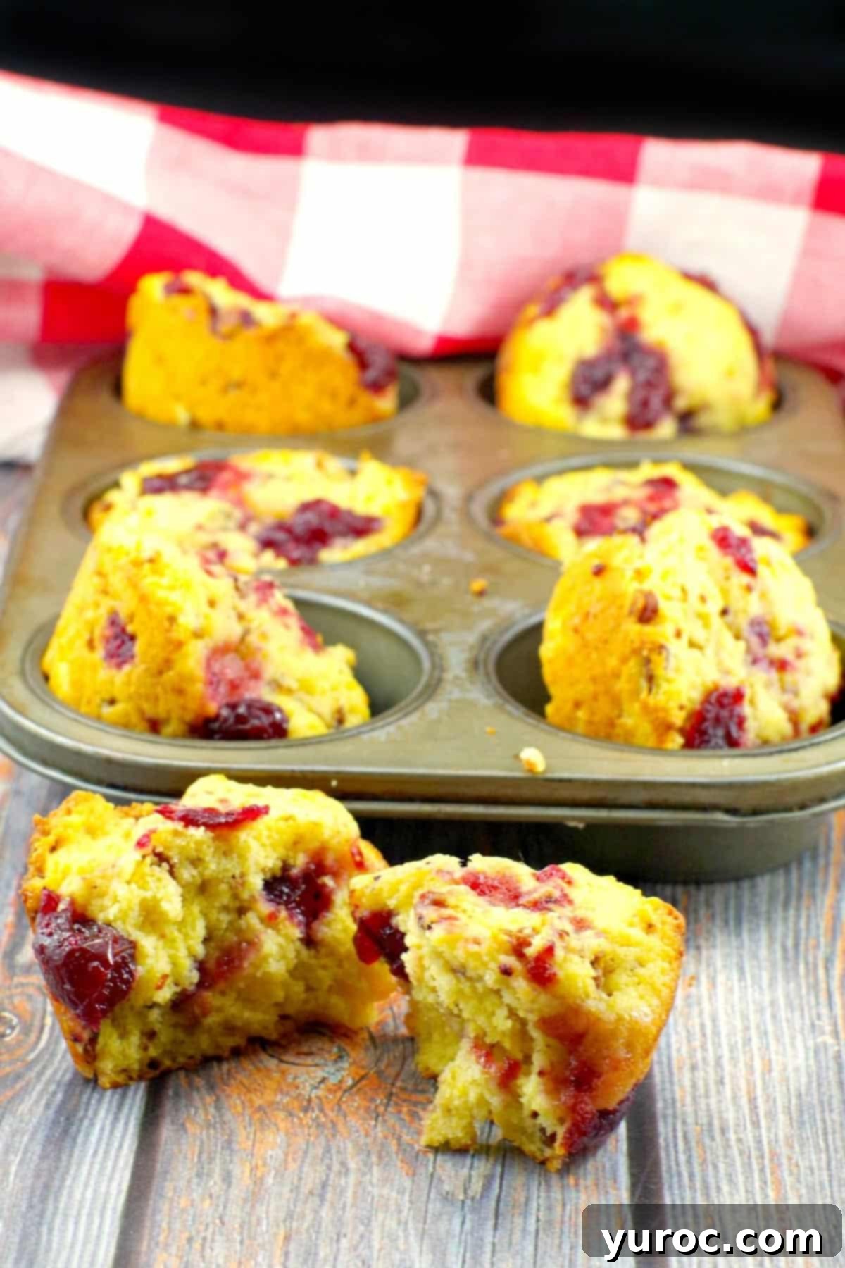 cranberry cornbread muffin spilt in half with a tin of muffins in the background