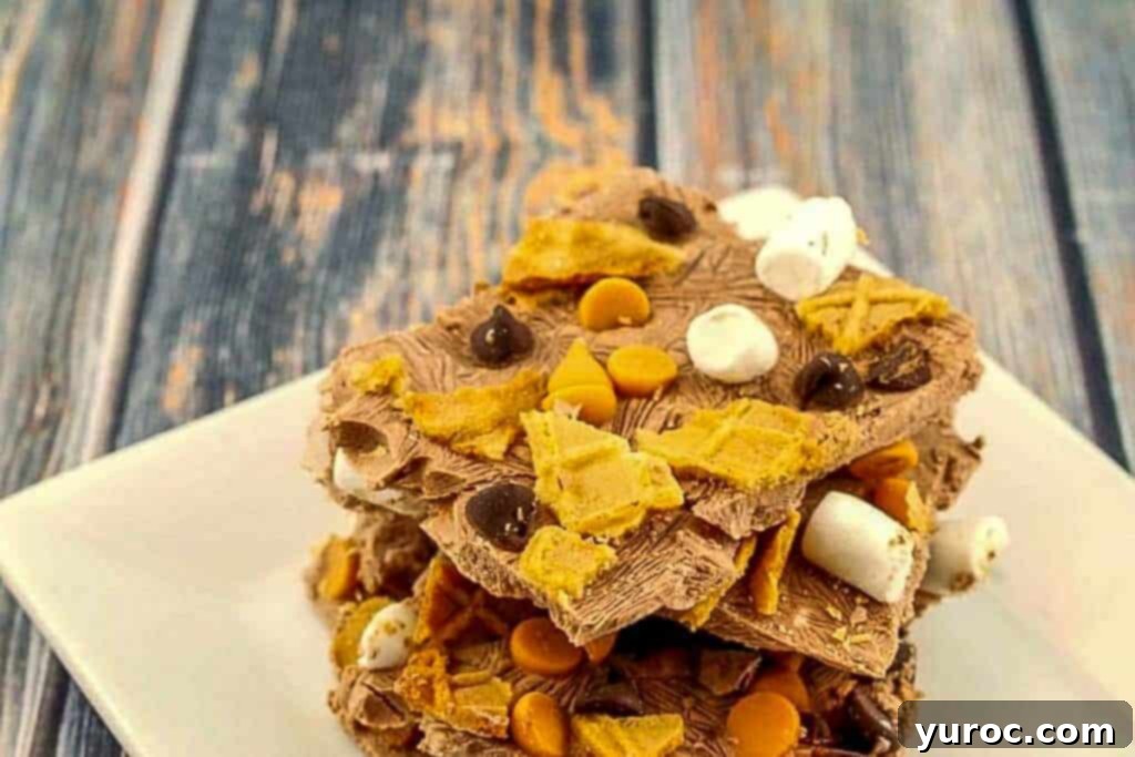 Multiple pieces of dark chocolate frozen Greek yogurt bark, topped with marshmallows, chocolate chips, and waffle cone fragments, neatly stacked on a pristine white plate, ready for serving.