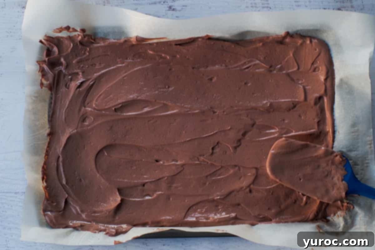 A spatula smoothly spreading rich chocolate yogurt onto a parchment-covered baking sheet, forming an even layer.