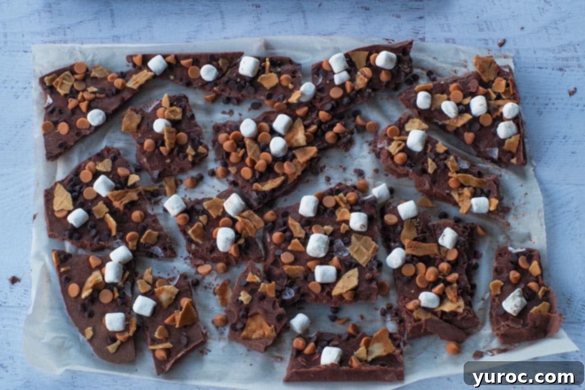A large sheet of Rocky Road Greek Frozen Yogurt Bark, perfectly frozen and broken into rough, appealing pieces directly on the parchment paper, showcasing its diverse toppings.