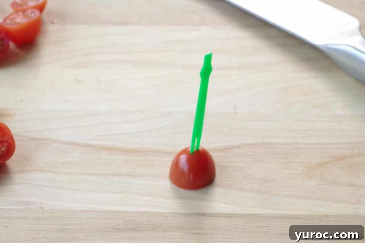 ½ a grape tomato on wooden cutting board with a skewer through the top of it