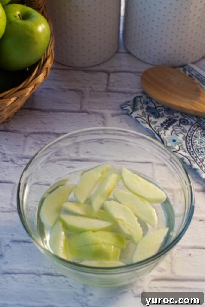 sliced apples in a glass bowl with lemon and water on white surface