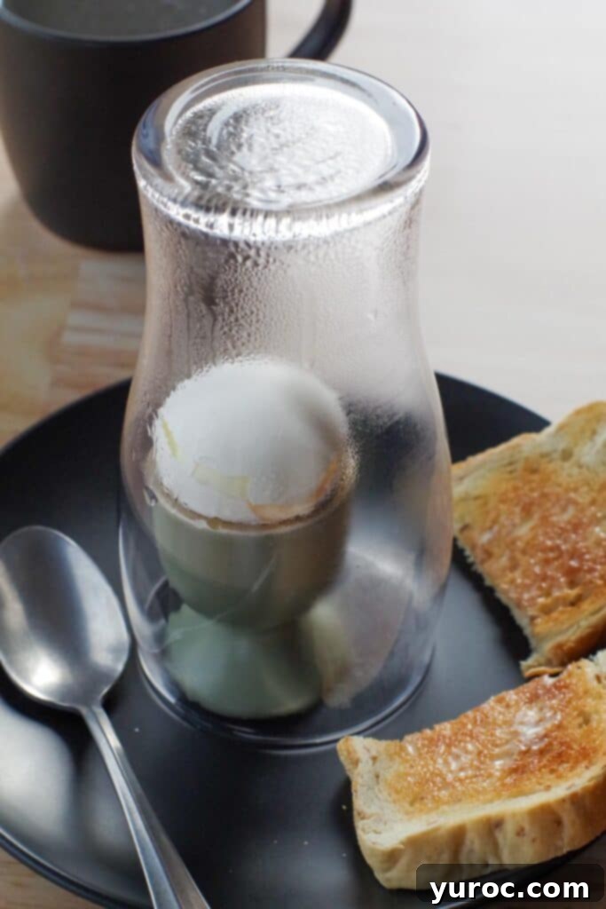 soft-boiled egg under a glass with toast on the side and spoon on other side