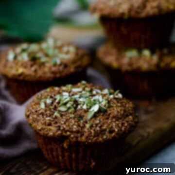 15 Deliciously Healthy Bran Muffin Recipes 12 Four perfectly baked zucchini bran muffins, artfully arranged on a rustic dark wooden cutting board, showcasing their enticing golden-brown tops and promising a moist, flavorful interior.