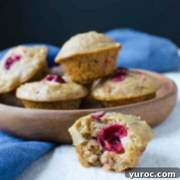 15 Deliciously Healthy Bran Muffin Recipes 5 A beautifully presented fruit and nut bran muffin, sliced in half to reveal its rich, wholesome interior with visible pecans, apple chunks, and cranberries, set against a blurred background of more tempting muffins.