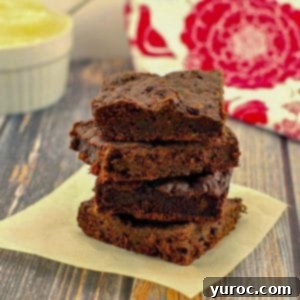 Sneaky Spinach Applesauce Brownies 14 4 brownies with spinach stacked on a piece of parchment paper with applesauce and a red and white tea towel in the background