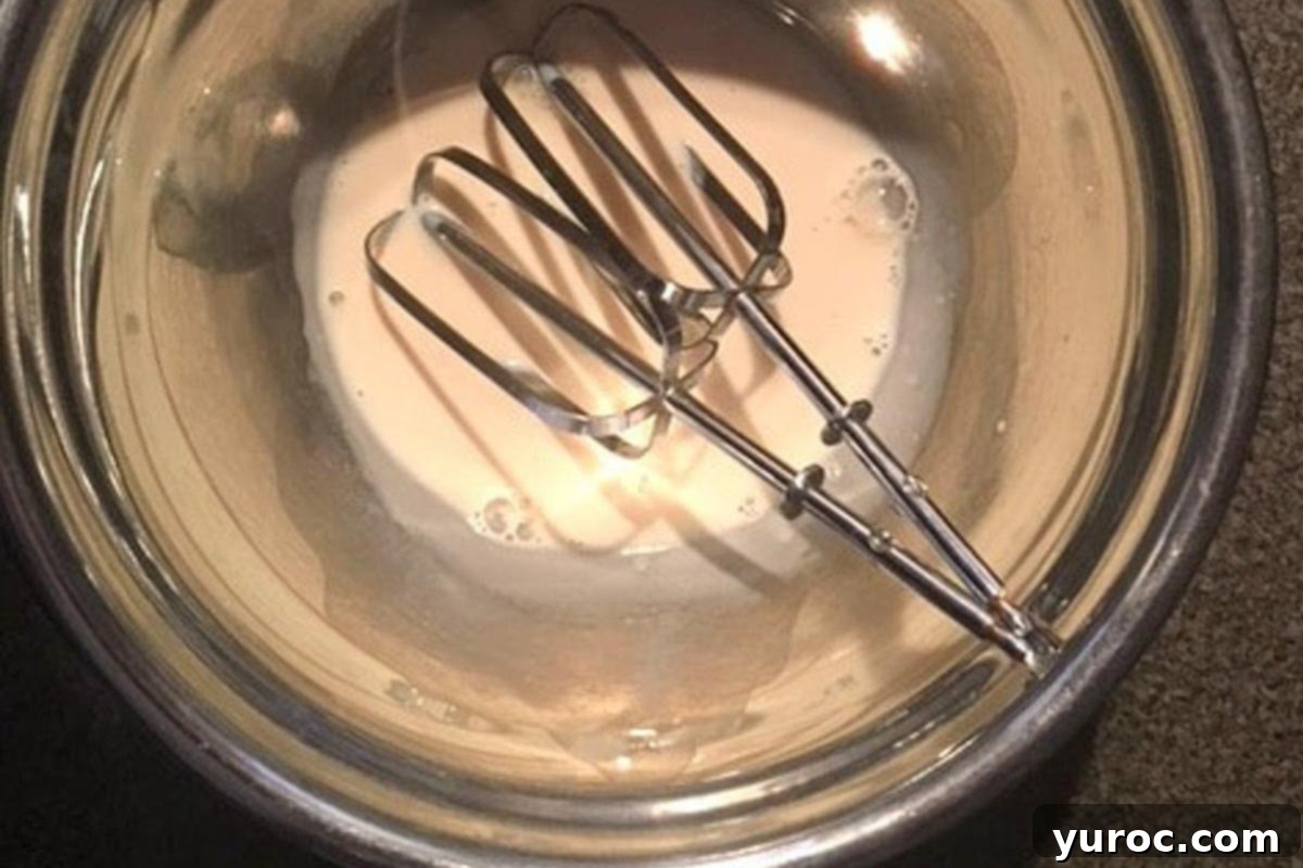 Evaporated milk in a metal bowl with electric beaters, ready for whipping