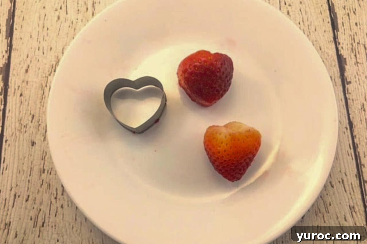 Strawberries being cut into heart shapes with a small cookie cutter